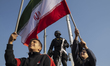 Two young Iranian boys wave country flags while sitting on an armored military vehicle dur...