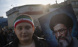 A young Iranian boy wearing a country flag stands beside a portrait of Iran's Supreme Lead...
