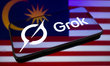 The Grok logo appears on the screen of a smartphone placed on a surface reflecting the Mal...
