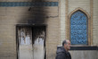 An Iranian man walks past the Aqsa Mosque, which burns during anti-government protests in...
