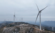 The giant wind turbines at Baiyunling Wind Farm slowly rotate with snow covering the turbi...