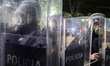 Three riot police officers in soaked protective gear stand during anti-government protests...