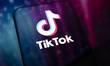 The TikTok logo is displayed on the screen of a smartphone placed on a reflective surface...