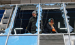 A man and a woman remove glass shards from a window shattered by an overnight Russian dron...
