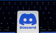 The Discord logo appears on the screen of a smartphone placed on a laptop keyboard illumin...