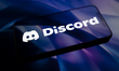 The Discord logo appears on the screen of a smartphone placed on a reflective surface onto...