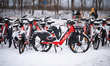 Snow-covered MEVO rental bicycles are parked at a bike-sharing station near beach entrance...