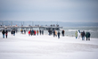 People walk on a snow-covered beach with the Brzezno Pier visible in the distance in Gdans...