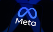 The Meta logo appears on a smartphone screen placed on a reflective surface onto which ano...