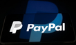 The PayPal logo appears on a smartphone screen placed on a reflective surface onto which t...