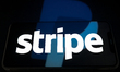 The Stripe logo appears on a smartphone screen placed on a reflective surface onto which a...