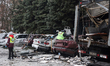 Public utility workers work beside vehicles damaged in a Russian strike drone attack in Kh...