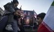 An Iranian family stands in front of a banner depicting portraits of the late Leader Ayato...
