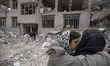 Two Iranian women hug each other while standing on the ruins of their apartment, which is...