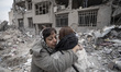 Two Iranian women hug each other while standing on the ruins of their apartment, which is...