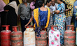 A woman rests on a liquefied petroleum gas (LPG) cylinder while waiting in a queue to buy...