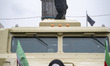 An Iranian family stands in front of an armored vehicle while an armed police officer moni...