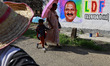 A woman with a child walks past a roadside wall featuring election graffiti depicting Left...