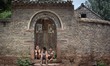 Children sit at a door of a courtyard in Linfeng village, a complex built with red rocks,...