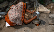 An elderly woman cooks rice on a newly built clay wood-fired stove in her house veranda wh...