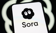 The Sora logo appears on a smartphone screen in front of a blurred OpenAI symbol in Cretei...