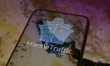 The MarineTraffic app logo is displayed on the screen of a smartphone placed on a reflecti...