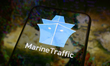 The MarineTraffic app logo is displayed on the screen of a smartphone placed on a reflecti...