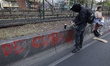 A protester spray-paints slogans on Calzada de Tlalpan against the inauguration of the Ban...