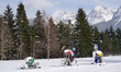 Snow cannons stand idle on a snow-covered field at the edge of a forest with the Karwendel...