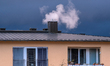 Smoke rises from a residential chimney above an apartment building under dark storm clouds...