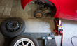 A red Citroen C1 is raised on a hydraulic jack during a wheel change, with one winter whee...