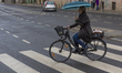 A woman rides a bicycle with an umbrella across a pedestrian crossing on Safarikova Street...