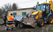 Men place debris into the bucket of a backhoe loader after a drone strike in Hatne, Kyiv r...
