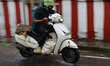 A man uses his hand to shield his eyes from the rain as he rides a scooter in Kochi, India...
