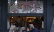 People sit outside a cafe with tape covering the windows to protect against shattering fro...