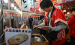 OSAKA, JAPAN - APRIL 4: 
 A vendor in a traditional red happi coat prepares 'Tamasen,' a...
