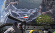 Two elderly Iranian men stand together beneath a giant billboard displaying an AI-generate...