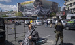 An armed Iranian policeman stands guard beneath a giant billboard displaying an AI-generat...