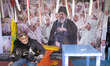 An elderly Iranian man sits in front of a banner depicting a portrait of Iran's late Supre...