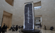 Visitors observe a large-scale digital screen installation featuring a high-tech reconstru...