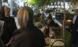 An Iranian man sits beside his parrot in a cage while resting on a bench along a sidewalk...