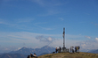 Hikers gather at a summit cross with snow patches near Neureuth and Gindelalmschneid in th...