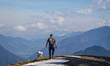 A hiker with a dog walks across snow patches and mountain trails near Neureuth and Gindela...