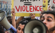 A demonstrator holds a placard reading, ''systemic racism = Violence'' while others shout...