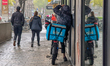 A Wolt bicycle courier shelters under a storefront roof during rain in Munich, Bavaria, Ge...