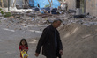 An elderly Iranian man and a young girl walk past the ruins of a destroyed building in the...