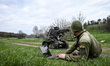A soldier lies on the ground beside a laptop as a machine gun mounted on a ground robotic...