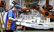 Workers cooperate with robots to produce automotive body sheet metal products in a mold st...