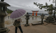 MIYAJIMA, JAPAN - APRIL 15: 
 A visitor with an umbrella looks toward the iconic 'floatin...