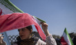 An Iranian woman sits beneath a national flag as she arrives to participate in a pro-gover...